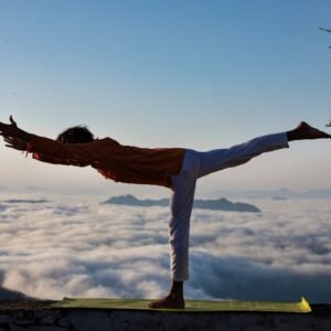 Person practicing yoga in warrior pose above a scenic cloudscape during sunrise.