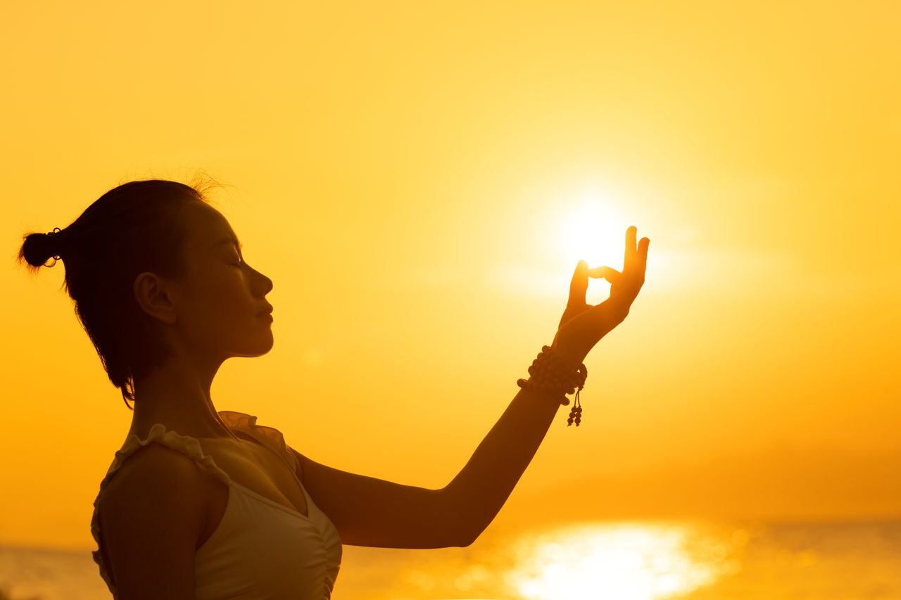 Silhouette of a woman meditating by the sea during a vibrant sunset, creating a peaceful atmosphere.