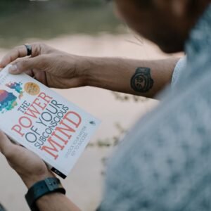A man reads 'The Power of Your Subconscious Mind' by a riverside, showcasing relaxation and reflection.