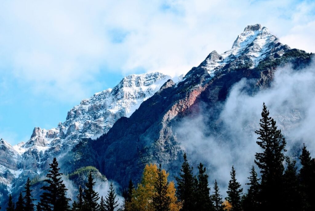 Scenic view of snow-capped mountains with mist and trees in the foreground, perfect for nature lovers.