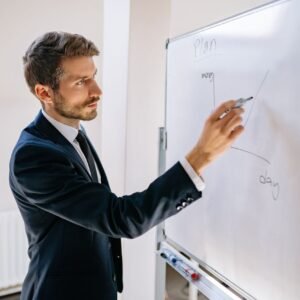 Executive in suit writing on whiteboard, explaining business graph.
