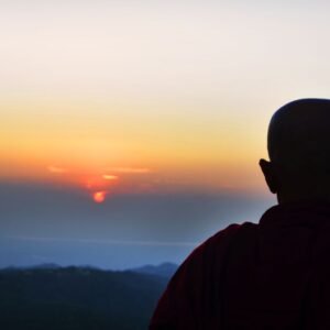 Silhouette of a monk overlooking a serene sunset on a mountain in Myanmar, capturing tranquility.