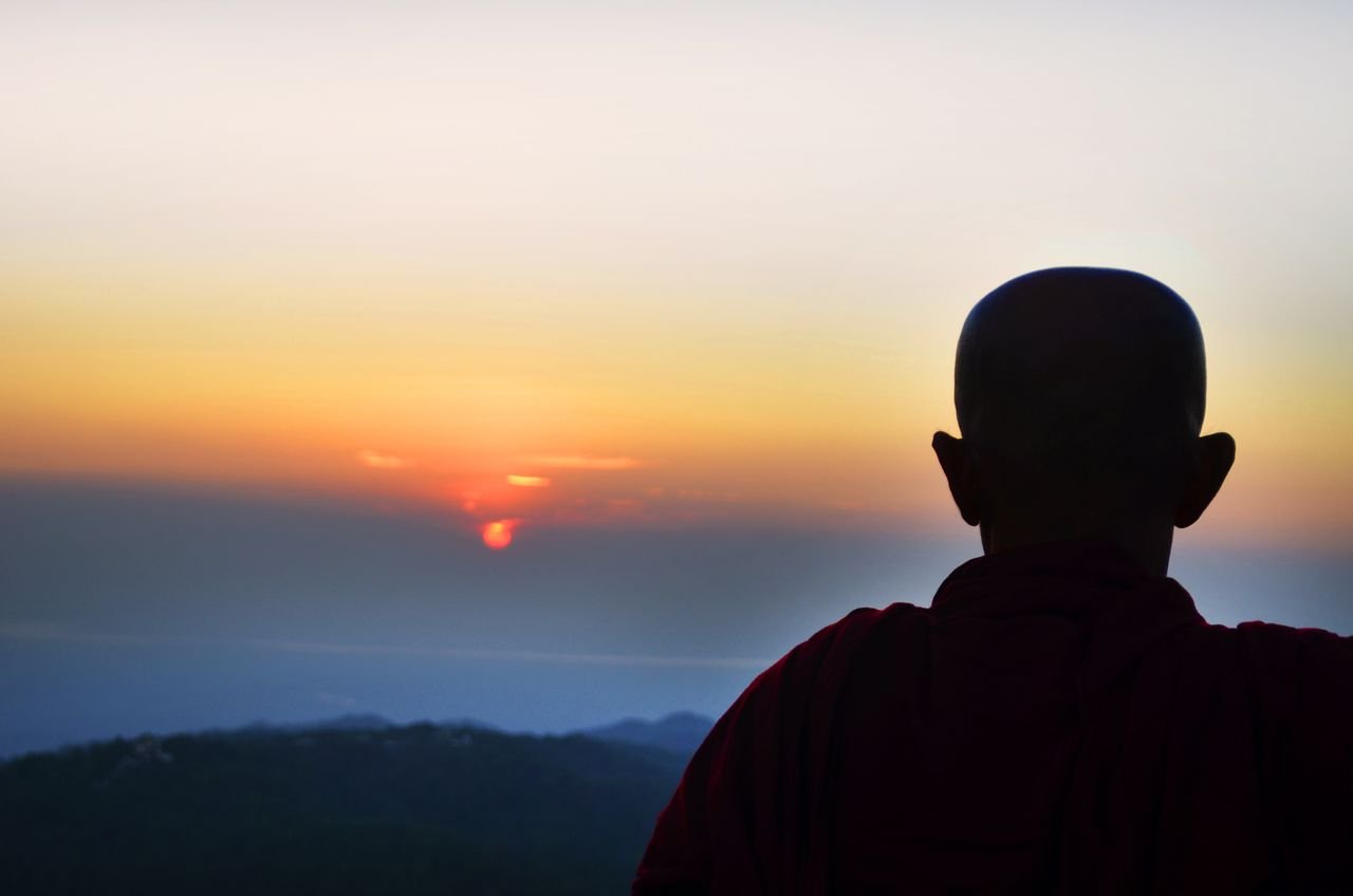 Silhouette of a monk overlooking a serene sunset on a mountain in Myanmar, capturing tranquility.